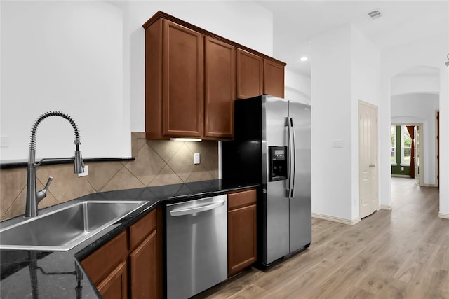 kitchen with a sink, appliances with stainless steel finishes, decorative backsplash, and arched walkways