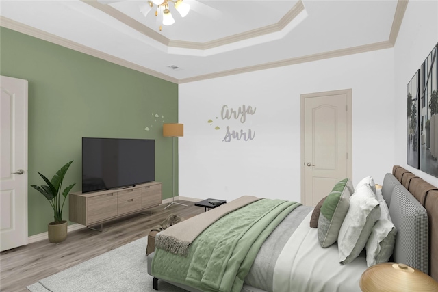 bedroom with a ceiling fan, baseboards, wood finished floors, a tray ceiling, and ornamental molding