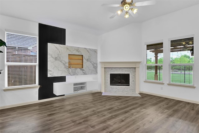 unfurnished living room featuring a ceiling fan, baseboards, wood finished floors, and a high end fireplace