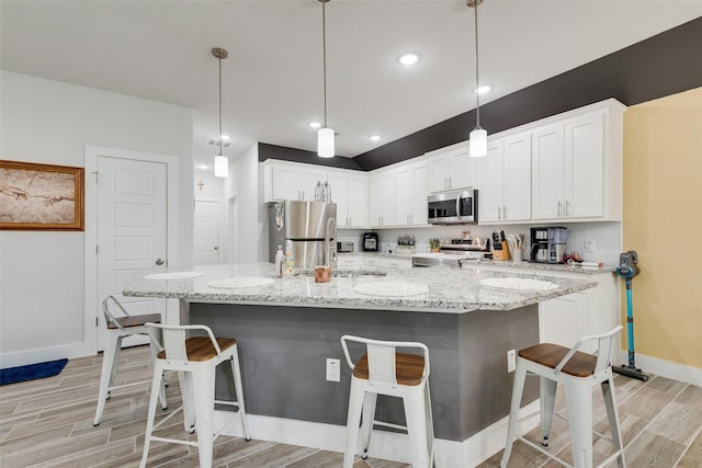 kitchen with light wood-style flooring, white cabinets, a breakfast bar, appliances with stainless steel finishes, and baseboards