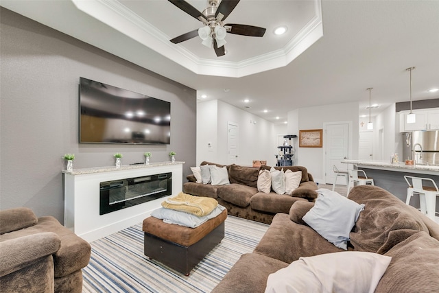 living room with a raised ceiling, crown molding, ceiling fan, and recessed lighting
