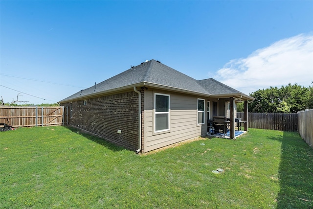 rear view of house featuring a shingled roof, a lawn, a fenced backyard, and brick siding