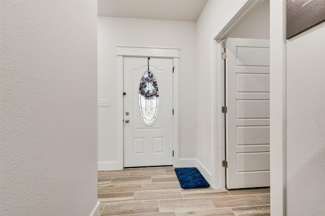 entryway featuring baseboards, a textured wall, and wood tiled floor