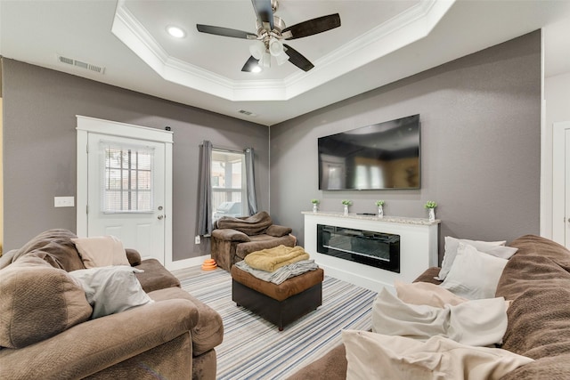 living area with crown molding, visible vents, a raised ceiling, and a ceiling fan