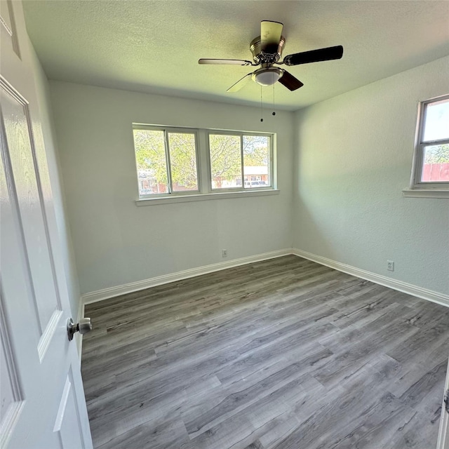empty room featuring a textured ceiling, wood finished floors, ceiling fan, and baseboards