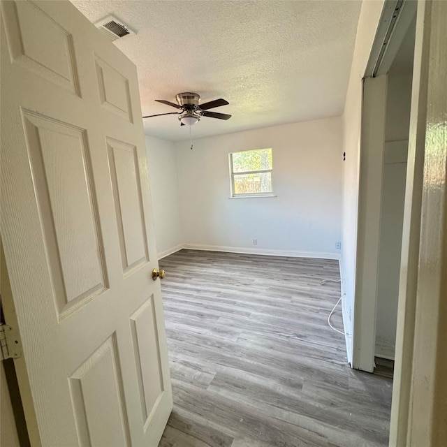 spare room with baseboards, a textured ceiling, visible vents, ceiling fan, and wood finished floors