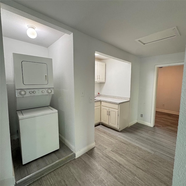 clothes washing area featuring laundry area, stacked washing maching and dryer, light wood-style floors, and baseboards