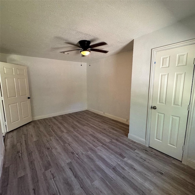 empty room with dark wood-type flooring, a textured ceiling, ceiling fan, and baseboards