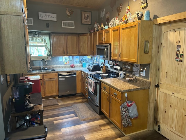kitchen featuring wood finished floors, stainless steel appliances, backsplash, a sink, and visible vents