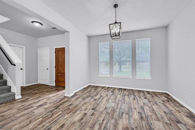 unfurnished dining area with visible vents, baseboards, an inviting chandelier, wood finished floors, and stairs