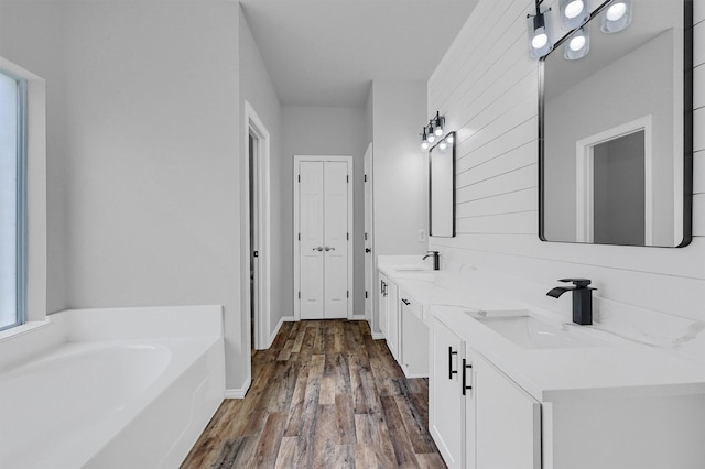 full bathroom featuring double vanity, wood finished floors, a garden tub, and a sink