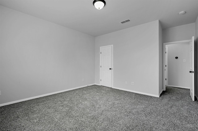 spare room featuring dark carpet, visible vents, and baseboards