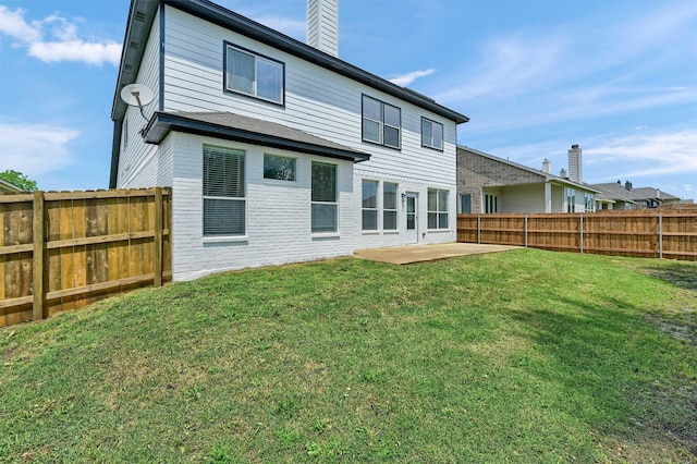 back of house featuring a chimney, a yard, a patio, and a fenced backyard
