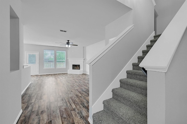 stairs with visible vents, baseboards, a brick fireplace, wood finished floors, and a ceiling fan