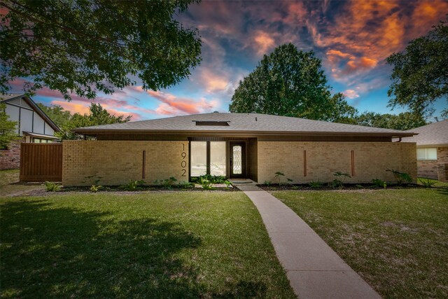 view of front of home with brick siding, a shingled roof, and a front yard