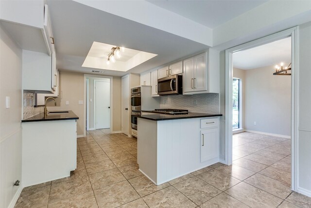 kitchen featuring a sink, decorative backsplash, stainless steel appliances, a raised ceiling, and a peninsula