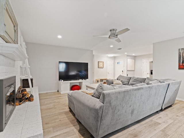 living room with ceiling fan, a brick fireplace, recessed lighting, baseboards, and light wood-type flooring