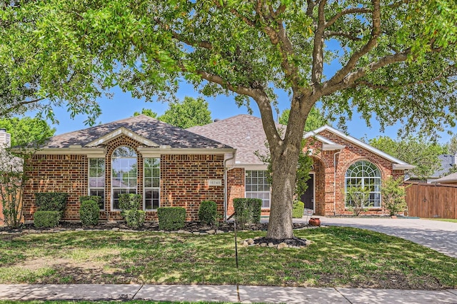 view of front facade with fence, roof with shingles, a front lawn, and brick siding