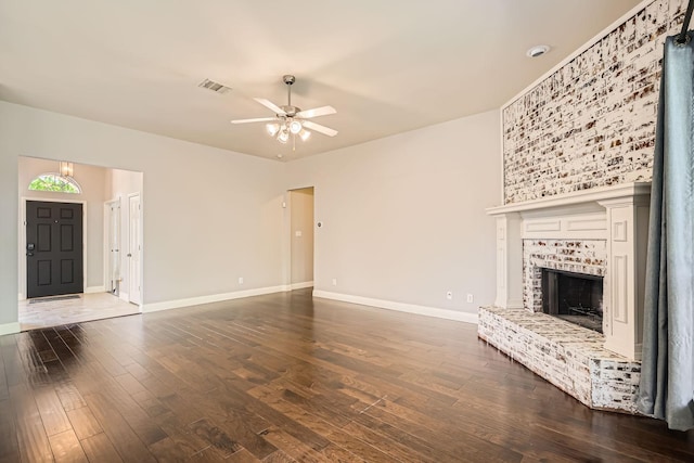 unfurnished living room featuring dark wood-style flooring, a brick fireplace, a ceiling fan, baseboards, and visible vents