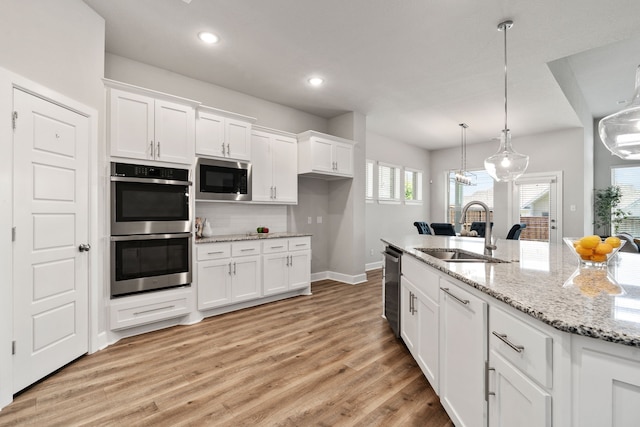 kitchen featuring light wood-style floors, white cabinets, appliances with stainless steel finishes, a sink, and baseboards
