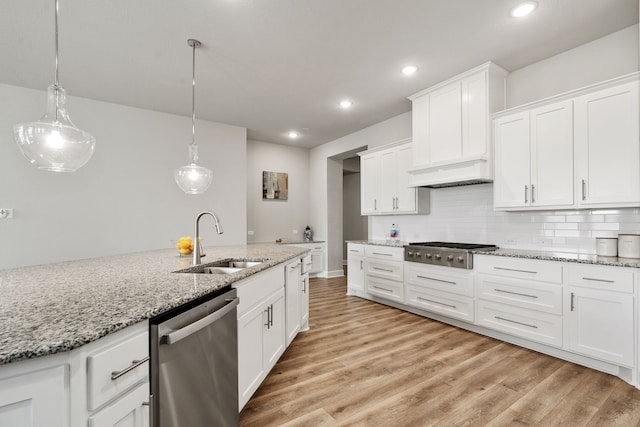 kitchen featuring stainless steel appliances, light wood finished floors, a sink, and backsplash