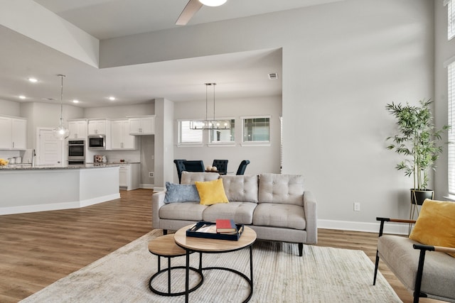 living room featuring light wood-style floors, ceiling fan with notable chandelier, visible vents, recessed lighting, and baseboards