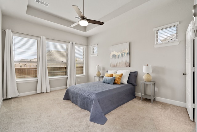 carpeted bedroom with a raised ceiling, ceiling fan, baseboards, and visible vents