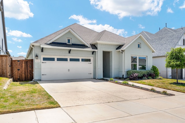 view of front facade with a shingled roof, an attached garage, fence, a front lawn, and driveway