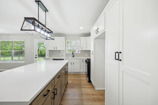 kitchen with black range with gas stovetop, a kitchen island, a sink, light countertops, and decorative backsplash