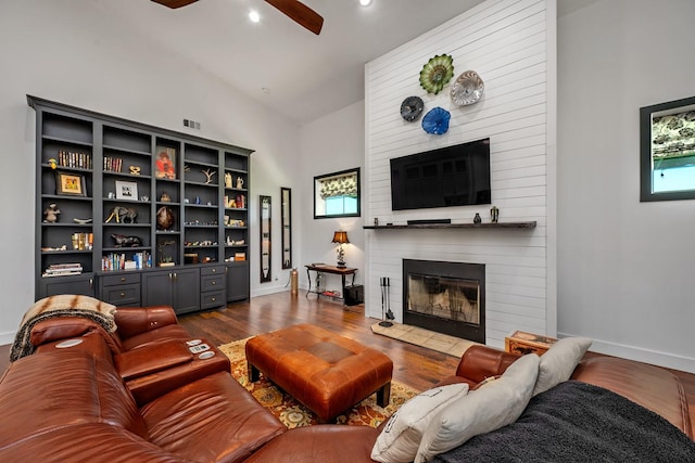 living room featuring visible vents, baseboards, dark wood-type flooring, a large fireplace, and a ceiling fan