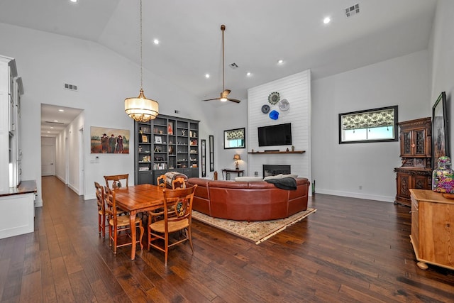 dining area featuring a brick fireplace, high vaulted ceiling, dark wood finished floors, a ceiling fan, and visible vents