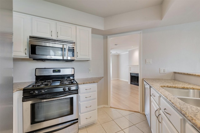 kitchen with appliances with stainless steel finishes, white cabinetry, a fireplace, light tile patterned flooring, and light stone countertops