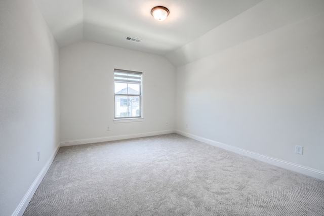carpeted empty room with visible vents, baseboards, and vaulted ceiling