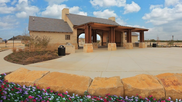rear view of house featuring a shingled roof, stone siding, a patio, and a chimney