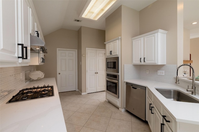 kitchen featuring light tile patterned floors, white cabinets, a sink, appliances with stainless steel finishes, and under cabinet range hood