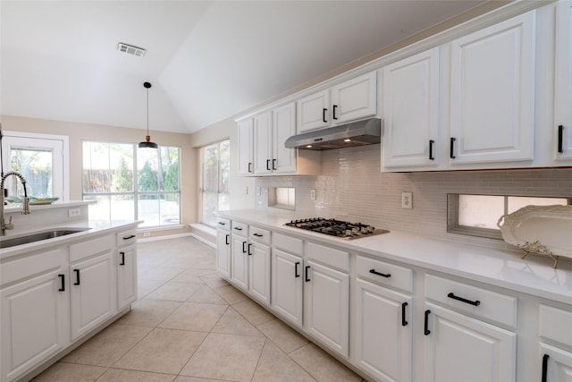kitchen featuring stainless steel gas stovetop, vaulted ceiling, under cabinet range hood, a sink, and backsplash