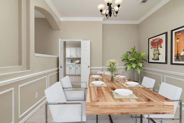 dining area with a decorative wall, ornamental molding, a wainscoted wall, and a notable chandelier
