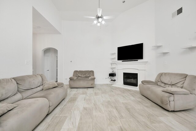 living room with visible vents, arched walkways, ceiling fan, high vaulted ceiling, and a glass covered fireplace