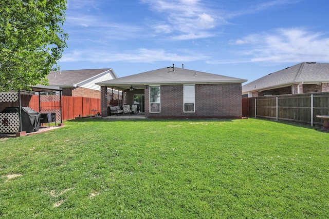 back of property with a lawn, ceiling fan, a fenced backyard, and brick siding