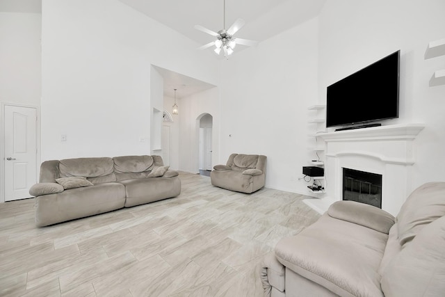living room with a fireplace with flush hearth, arched walkways, high vaulted ceiling, and ceiling fan