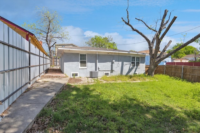 back of house featuring central AC unit, stucco siding, fence, and a lawn