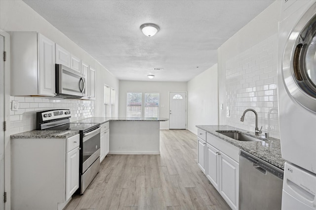 kitchen with light wood-style floors, a sink, stainless steel appliances, backsplash, and stacked washer / drying machine