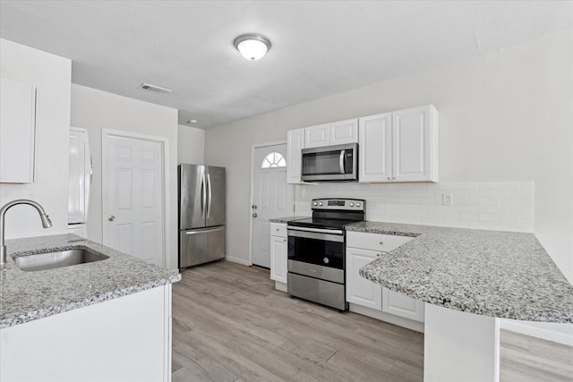 kitchen with light wood-style floors, a peninsula, visible vents, appliances with stainless steel finishes, and a sink