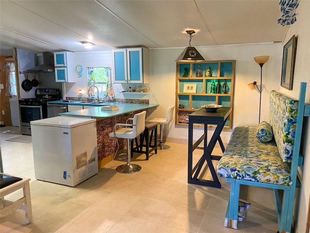 kitchen featuring stainless steel range with gas stovetop, wall chimney exhaust hood, a peninsula, refrigerator, and a sink