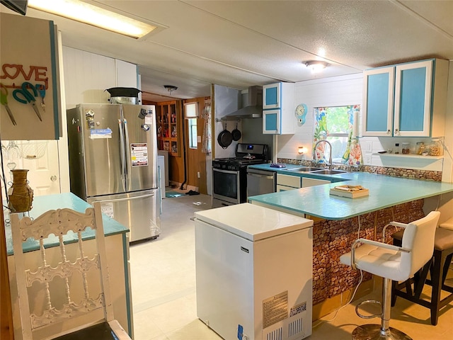 kitchen with a kitchen breakfast bar, a peninsula, wall chimney exhaust hood, stainless steel appliances, and a sink