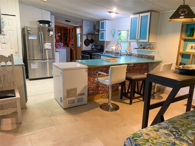 kitchen with a peninsula, a breakfast bar, light tile patterned flooring, a sink, and stainless steel appliances