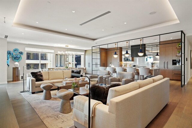 living room featuring recessed lighting, a raised ceiling, a notable chandelier, and wood finished floors