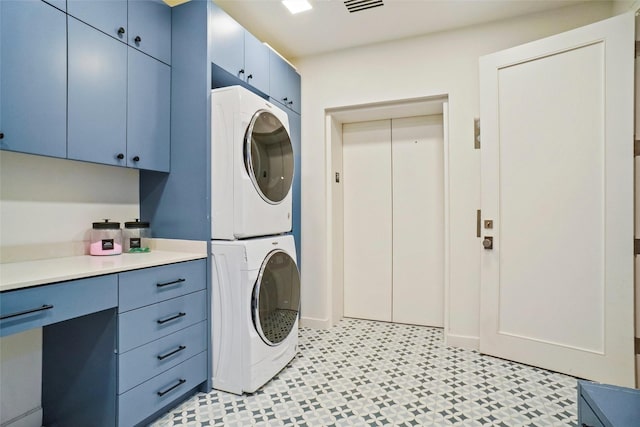 clothes washing area featuring stacked washer and dryer, cabinet space, and elevator