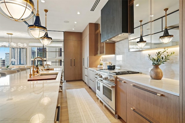 kitchen with double oven range, tasteful backsplash, a sink, light wood-type flooring, and wall chimney exhaust hood