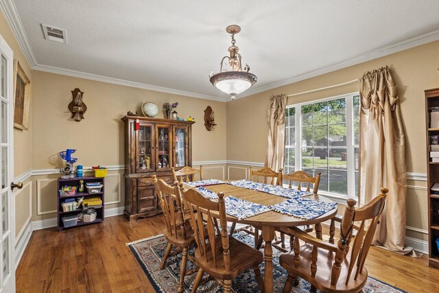 dining area featuring wood finished floors, visible vents, and crown molding